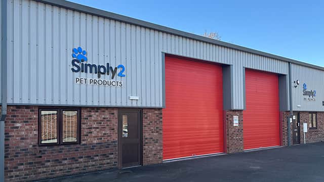 Exterior of Simply2 Pet Products with red garage doors, brick facade, and clear blue sky above.