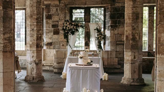 Elegant wedding setup with a decorated cake, floral arrangements, and candles in a historic stone building.