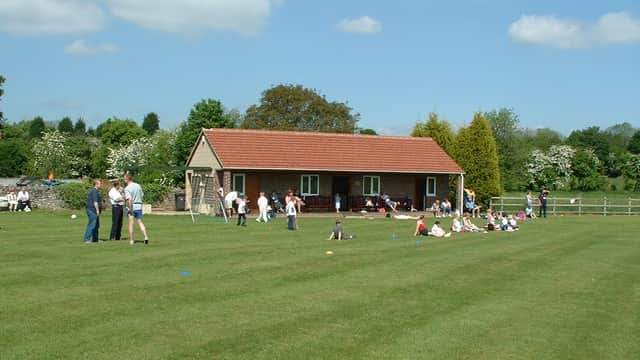 South Milford Cricket Club with a building, green field, and people enjoying outdoor activities on a sunny day.