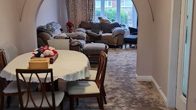 Dining area with a round table and chairs, leading to a cozy living room with a sofa and large windows.