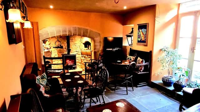 Cozy interior of The Fox & Hounds Inn, featuring a stone fireplace, wooden furniture, and warm orange walls.