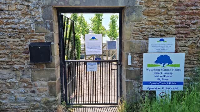 Entrance gate to Wykeham Mature Plants with signs about services and business hours, surrounded by stone walls and greenery.