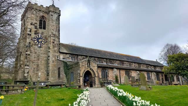 St. Andrew's Church with a stone tower, clock, and daffodils lining the path in a tranquil Yorkshire setting.