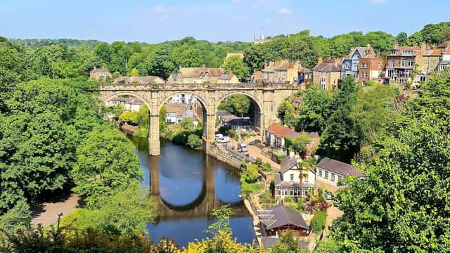 Scenic view of Knaresborough with a river, lush greenery, and a historic stone viaduct in the background.
