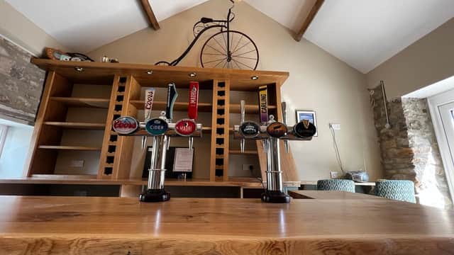 Bar counter with various beer taps, wooden shelves, and a vintage bicycle hanging from the ceiling in a cozy setting.