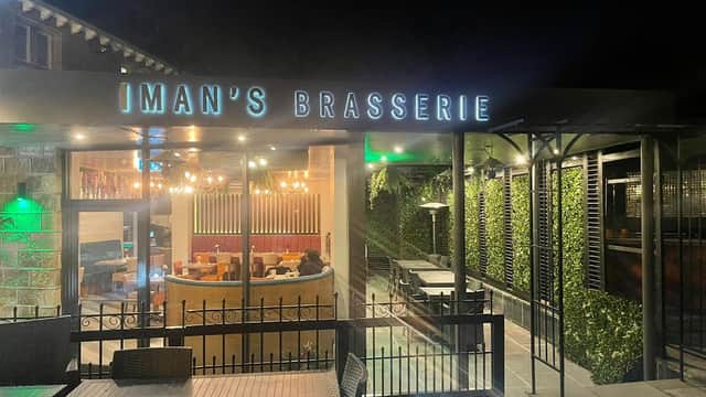 "Iman's Brasserie sign illuminated at night, with outdoor seating and green foliage in a cozy setting."