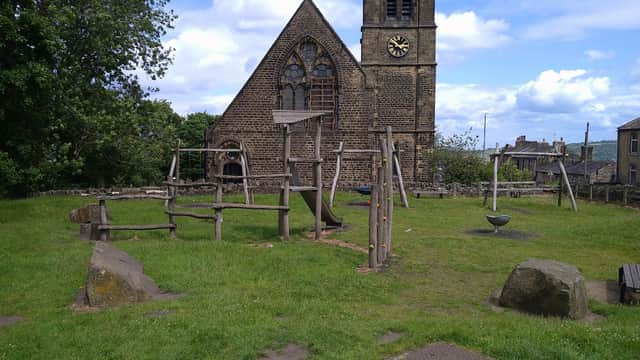 Playground equipment in a grassy area near a historic stone church with a clock tower and cloudy blue sky.