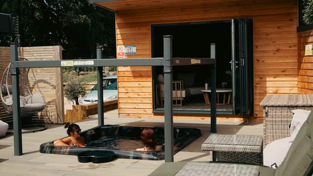 Two women relax in a hot tub outside a wooden spa building with patio furniture and greenery in Welton, Yorkshire.