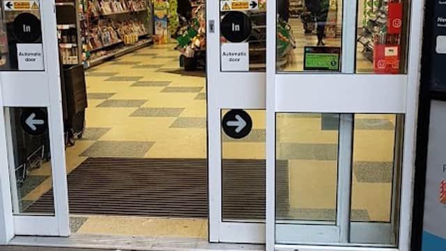 Entrance to Co-op Food with shopping aisles visible, shoppers inside, and signage on glass doors.