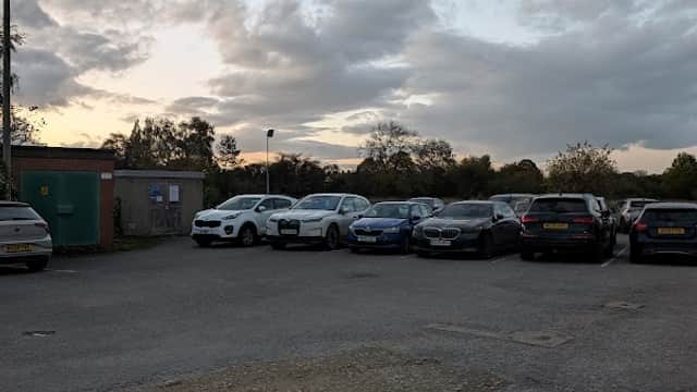 Car park with various parked cars, cloudy sky, and a green utility shed in the background.