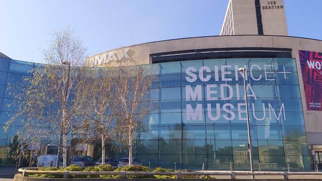 Modern glass building with large signage reading "Science + Media Museum," surrounded by trees and urban architecture.