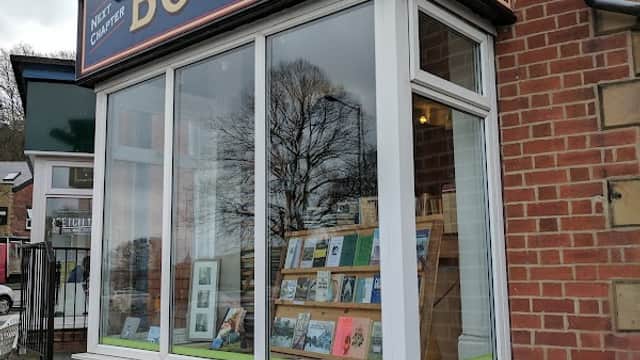 Bookshop storefront with large sign "Next Chapter Books" and display of books in the window. Red brick building.