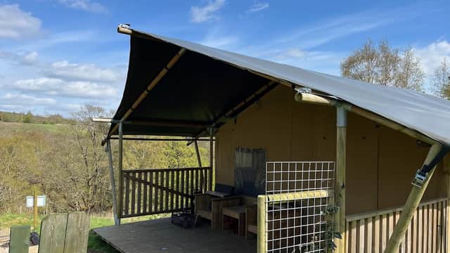Glamping tent with a wooden deck, surrounded by trees and a blue sky in Secret Valley Escapes, Holme Valley.