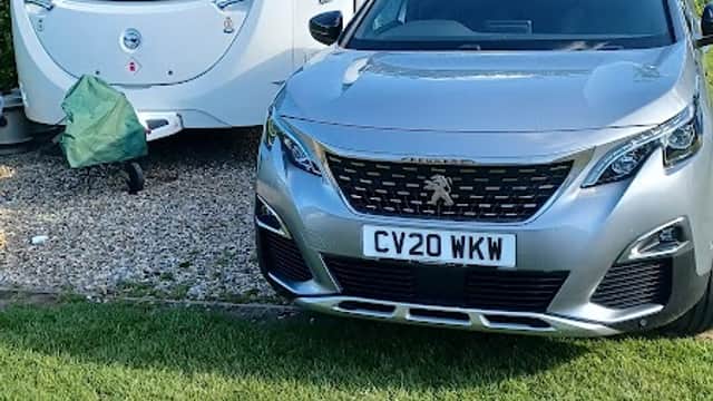 Caravan parked on gravel with a silver car in front, surrounded by greenery at St Helens Caravan Park, Hutton Buscel.