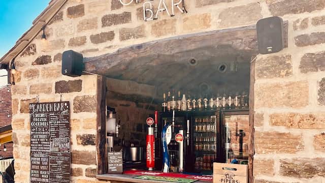 Rustic stone exterior of The Wentworth Arms with a garden bar and a menu board featuring drinks and cocktails.