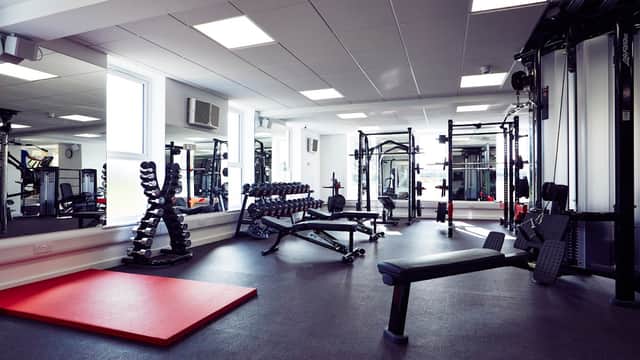 Modern gym interior featuring weightlifting equipment, benches, dumbbells, and a red exercise mat.
