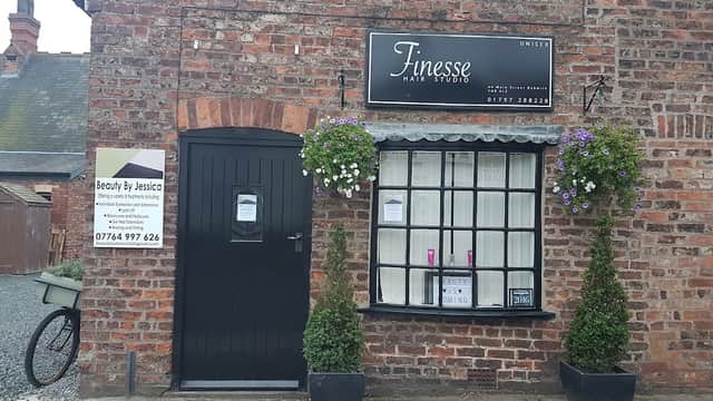 Brick building with a black door, window with flower baskets, and a sign for "Finesse Hair Studio" and "Beauty By Jessica."