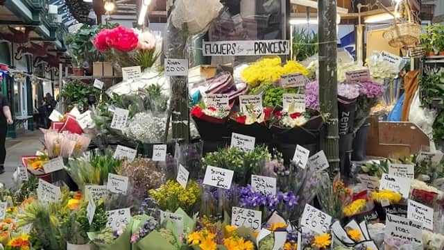 Colorful flower display with various bouquets, price tags, and a sign reading "M and D Flowers" in a market setting.