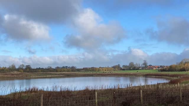 Serene lake surrounded by lush greenery and distant houses under a partly cloudy sky in Scorton, North Yorkshire.