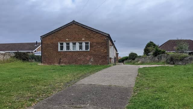 Fairburn Old Church Hall, a brick building with multiple windows, set on a grassy area with a concrete path leading up to it.