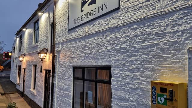 The Bridge Inn bar with whitewashed walls, lanterns, and a defibrillator box outside, set in Ruswarp, Yorkshire.