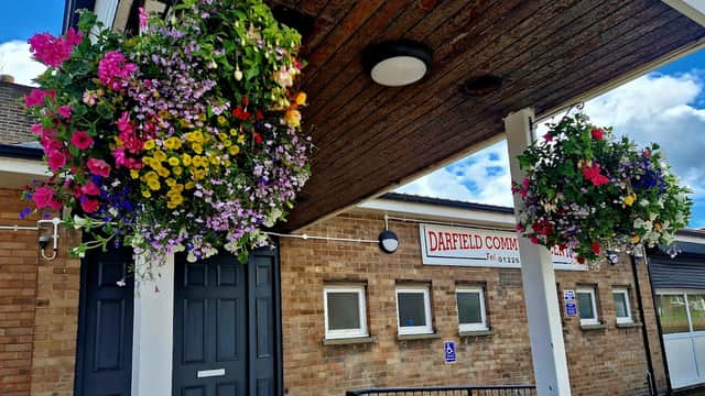 Colorful hanging flower baskets adorn the entrance of Darfield Community Centre, featuring a brick faΓ§ade and signage.