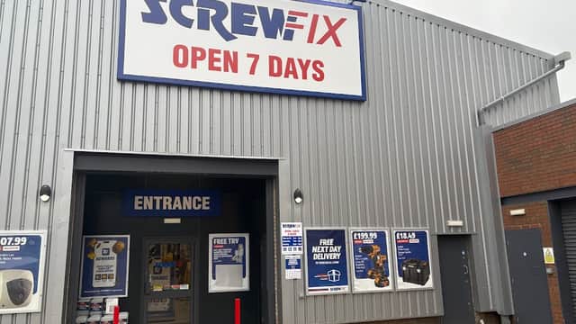 Screwfix store exterior with large sign, entrance doors, and promotional banners on a gray building.