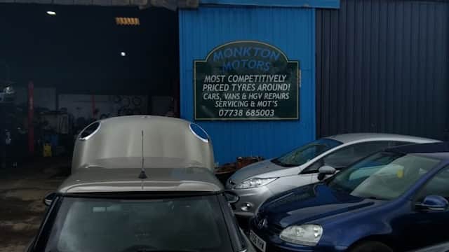 Sign for Monkton Motors on a blue wall, surrounded by parked cars in a garage setting.