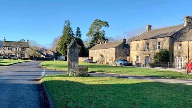 The Falcon Inn, a stone building, surrounded by green grass and trees, with nearby cottages and parked cars.