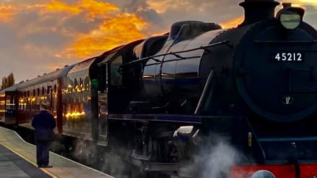 Steam train 45212 at Wensleydale Railway station, with a dramatic sunset and a person standing on the platform.
