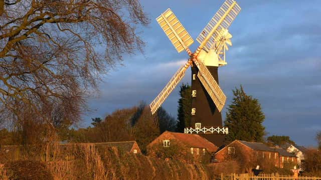 Skidby Mill stands tall with white sails, surrounded by lush greenery and a tranquil sky at sunset.