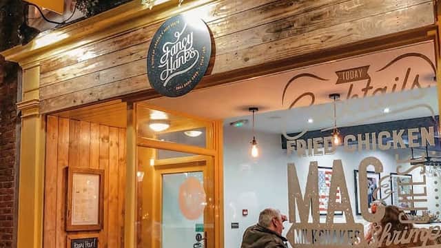 Brightly lit restaurant entrance with wooden accents, outdoor sign, and large glass windows showcasing diners inside.