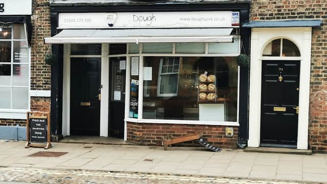 Quaint bakery "Dough" with large window displaying fresh bread, black doors, and cobblestone street in York, Yorkshire.