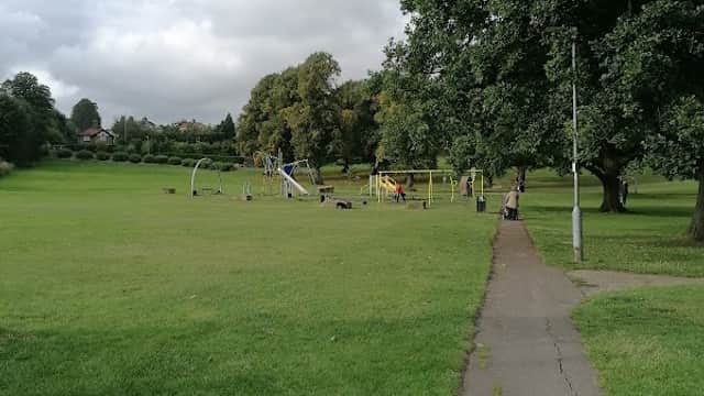 Lush green park with a pathway, playground equipment, and trees under a cloudy sky in Hipperholme, Yorkshire.