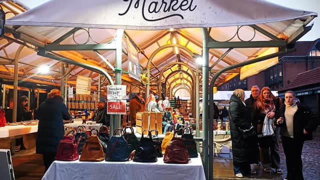 Stalls at Shambles Market display bags and food items, with shoppers browsing in a vibrant, bustling atmosphere.