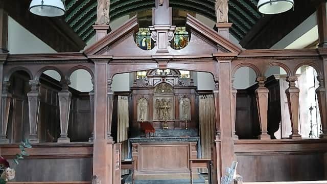 Interior of St Chad's Church featuring wooden pews, a crucifix, and stained glass above the altar.