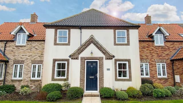 Charming two-story building with a dark door and white facade, surrounded by well-maintained gardens and blue sky.