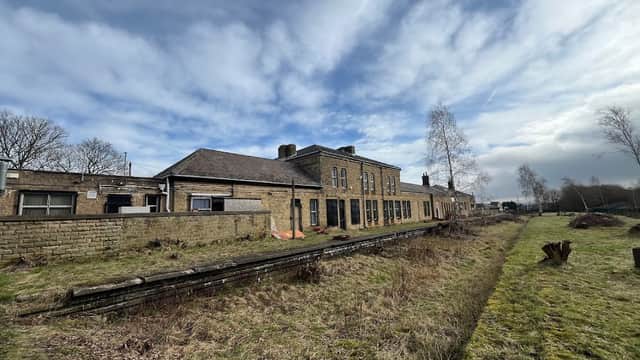 Historic railway station building with stone facade, overgrown tracks, and a cloudy sky in Penistone, Yorkshire.