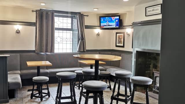 Cozy bar interior with wooden tables, high stools, a TV, and a fireplace, featuring gray walls and curtains.