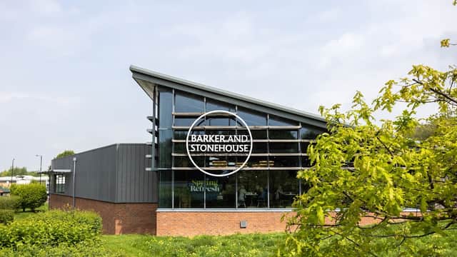 Modern furniture shop with large glass windows, featuring the sign "Barker and Stonehouse" surrounded by greenery.