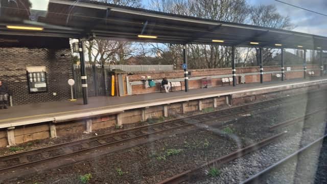 Wakefield Westgate Station platform with passengers, brick walls, and trees in the background under a cloudy sky.