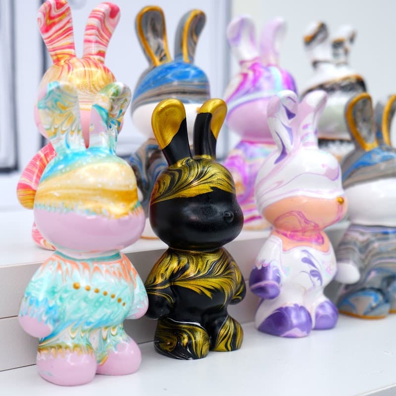 Colorful, decorative bunny figurines in various patterns and colors displayed on a shelf at MeowCraft gift shop.