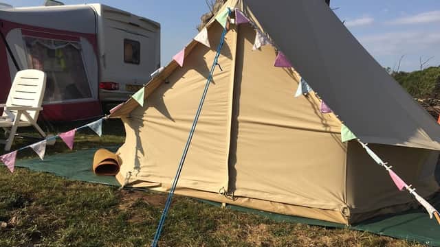 A beige tent with colorful bunting, a white chair, and a caravan in a grassy campsite under a clear blue sky.