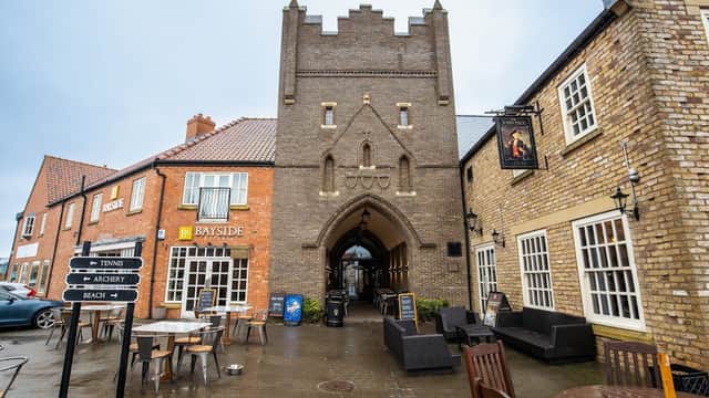 Meadowside House with a stone archway, shops, and outdoor seating in a coastal town setting.