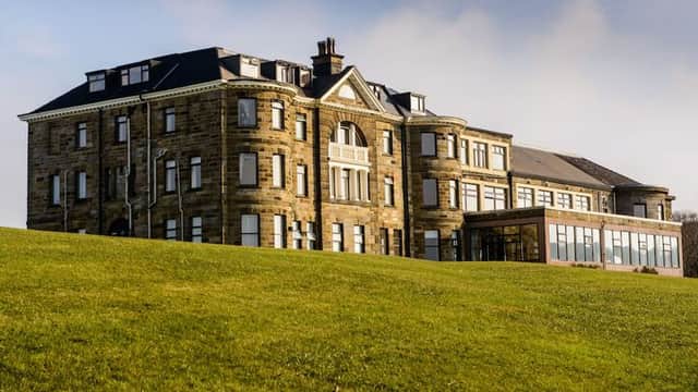 Historic stone mansion with large windows, surrounded by lush green lawn and a glass-enclosed extension.