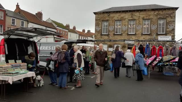 Busy market scene with people browsing stalls, a van, and colorful clothing hanging nearby in Great Broughton.