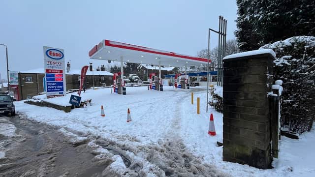 Esso gas station in Ovenden, Yorkshire, surrounded by snow, with visible fuel pumps and a sign indicating open hours.