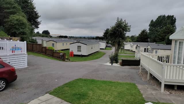 Caravans lined along a winding path, green lawns, and trees under a cloudy sky at Spring Willows Leisure Park.