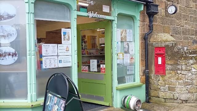 Green storefront of Thorpe Stores with a welcome sign, display windows, a blackboard menu, and a red post box nearby.