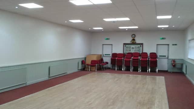 Spacious community hall with wooden floor, stacked red chairs, and bright lighting.